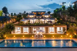 Villa nghỉ dưỡng Đồng Chanh Lake Ville lúc chạng vạng với hồ bơi, dãy phòng ngủ mở ra sân cỏ và mái xanh, Archiindex thiết kế