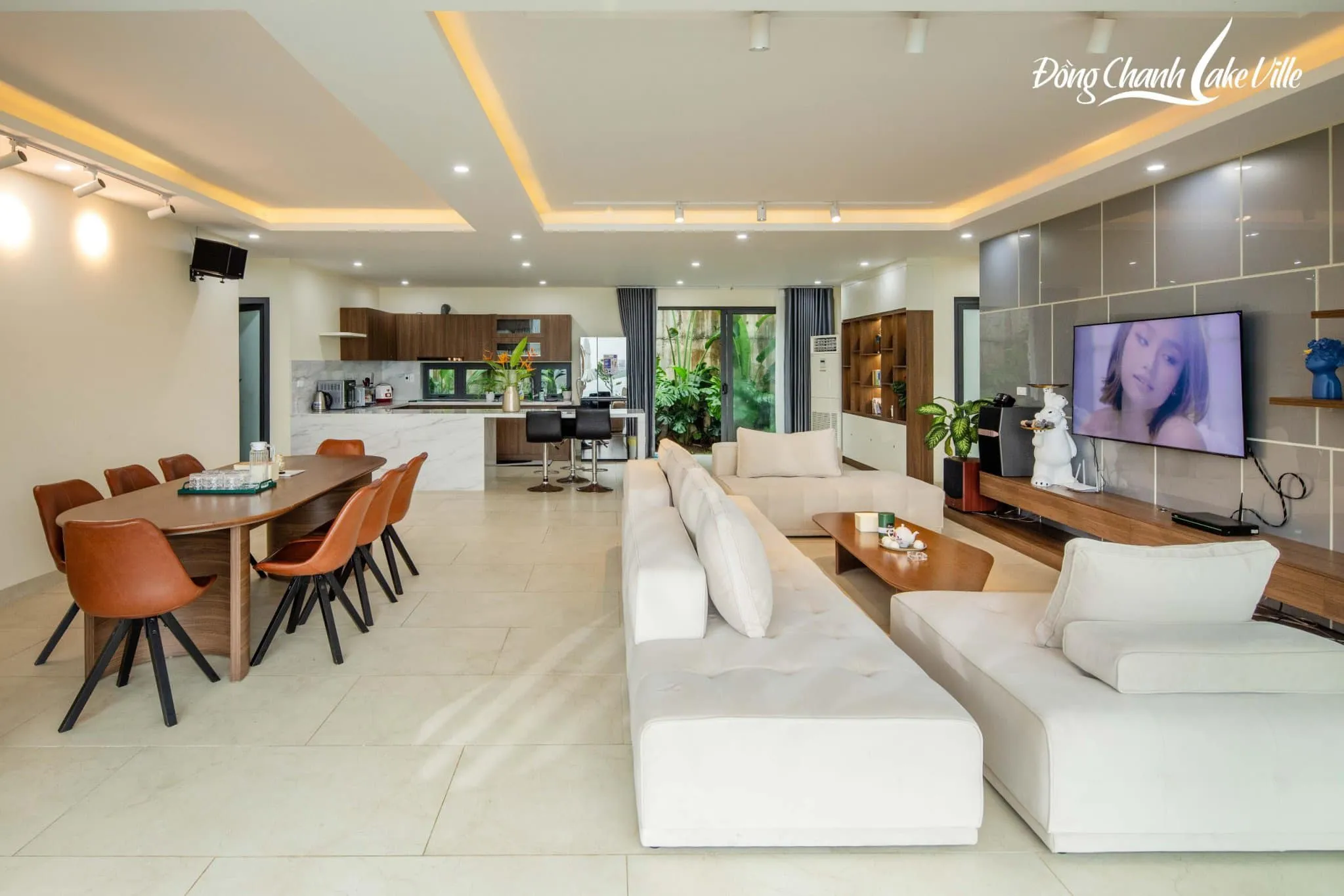 Phòng khách, bàn ăn dài và bếp mở trong villa Đồng Chanh Lake Ville, không gian sinh hoạt chung cho cả đoàn khách